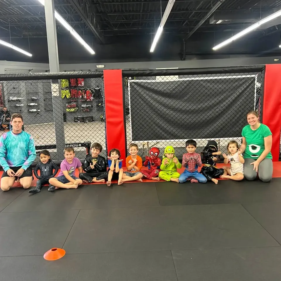 Little Monsters in superhero costumes sitting in a row on the mat with their coaches